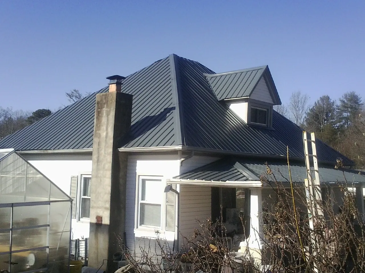Dark blue standing seam metal roof on a white farmhouse with dormer — Slate & Tile Roof Repair by Roofing Brothers in Drakesville