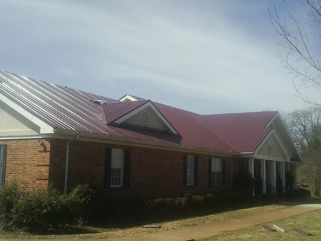 Red metal roof with gabled entries on a long brick building, from a Hail Damage Roof Repair job in Drakesville
