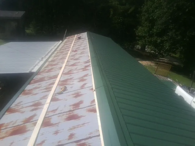 Old rusted panels beside newly installed green metal roofing — Wind Damage Roof Repair by Roofing Brothers in Drakesville