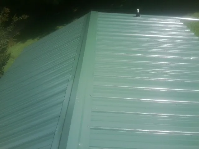 New green metal panels meeting at the ridge of a roof — Flat Roof Repair work by our crew in Drakesville
