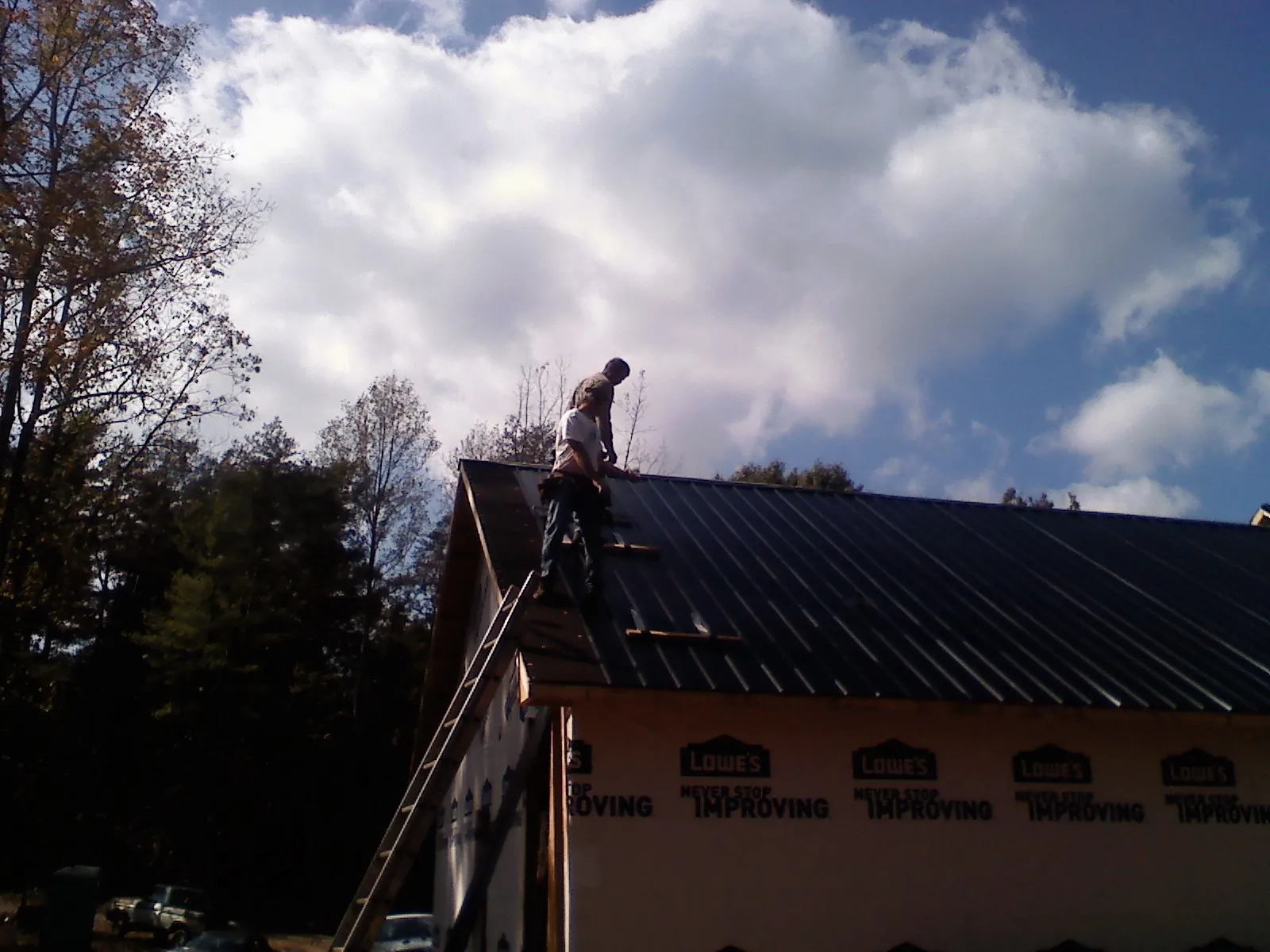 Roofer fastening dark metal panels high against a cloudy sky, from a Roof Inspection job in Drakesville