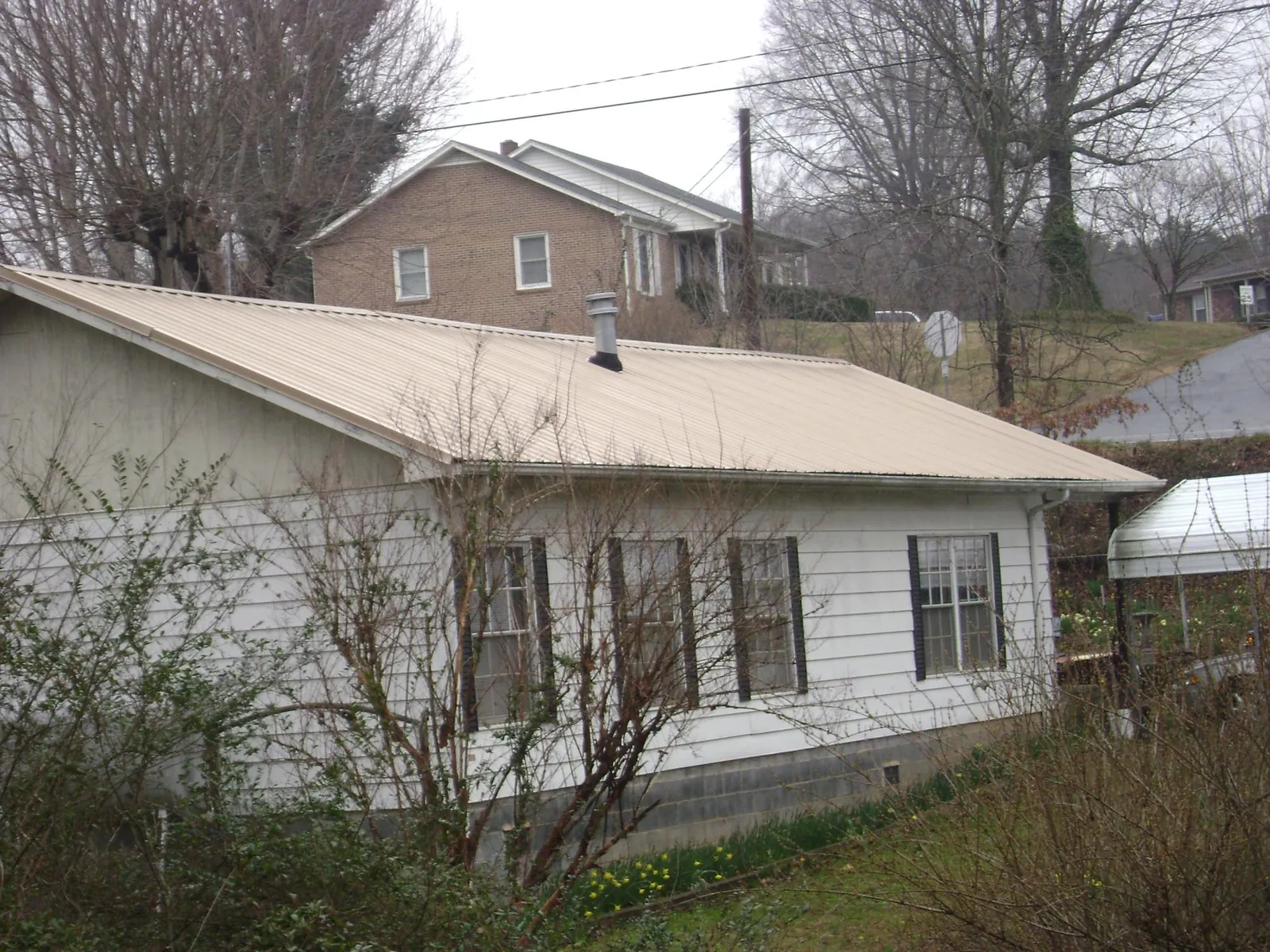 Tan metal roof on a white sided house set into a hillside — Commercial Roofing by Roofing Brothers in Drakesville