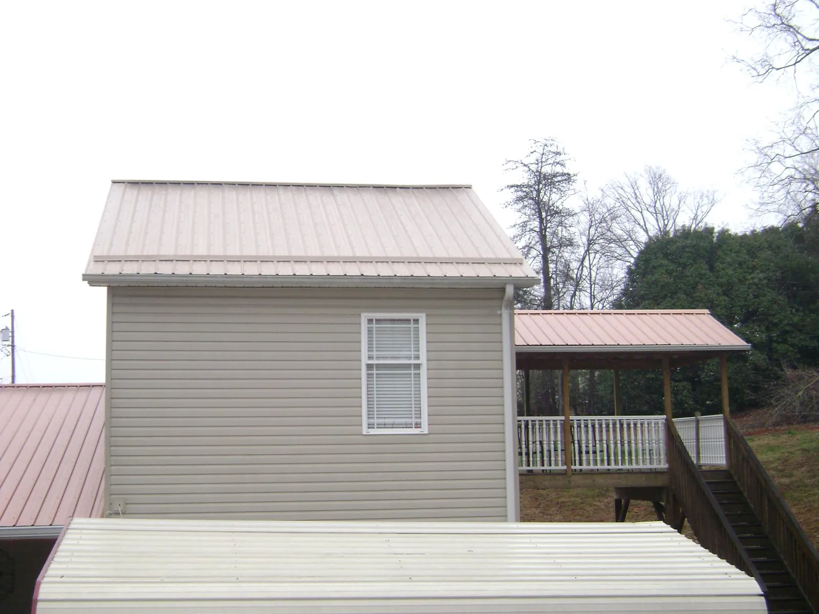 Tan metal roofs on a two story addition and attached porch, from a Roof Replacement job in Drakesville